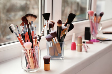 Set of makeup brushes and cosmetics on window sill