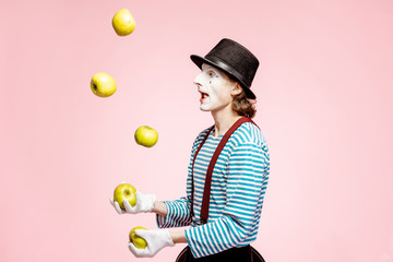 Pantomime with white facial makeup juggling with apples on the pink background in the studio - obrazy, fototapety, plakaty