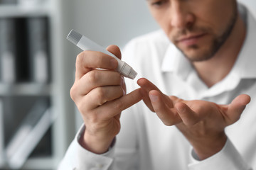 Diabetic man taking blood sample with lancet pen at home