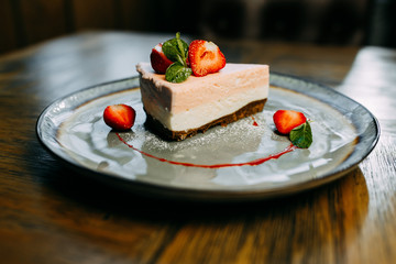 Cheese cake with strawberry and mint on the plate. Strawberry dessert. Reastaurant dishes on the wooden table. Food photo for restaurant menu. 