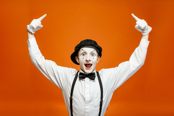 Emotional pantomime with white facial makeup showing empty space on the orange background,...
