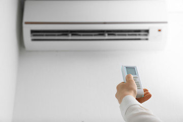 Fototapeta premium Young woman switching on air conditioner at home