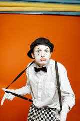 Portrait of an actor as a pantomime with white facial makeup showing expressive emotions on the orange background in the studio