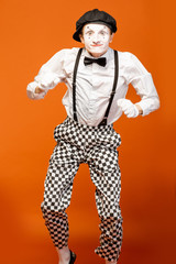 Portrait of an actor as a pantomime with white facial makeup showing expressive emotions on the orange background in the studio