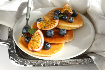 Plate with tasty pancakes, passion fruit and berries on tray