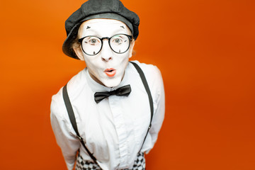 Portrait of an actor as a pantomime with white facial makeup showing expressive emotions on the orange background in the studio