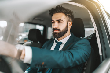 Portrait of caucasian bearded businessman in formal wear driving car.