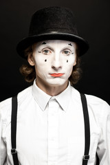 Close-up portrait of a pantomime with white facial makeup posing with expressive emotions on the black background