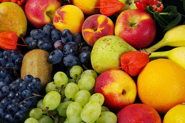 Naklejka na ściany i meble A variety of fruits on the dishes on the table. Grapes, peaches, bananas, kiwi, apples, lemon, orange, pomegranate, pears. Close-up.