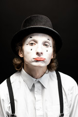 Close-up portrait of a pantomime with white facial makeup posing with expressive emotions on the black background