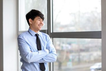 Fototapeta premium Portrait of young Asian businessman near window in office