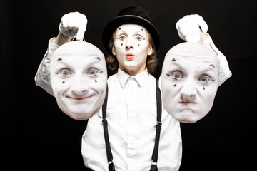 Portrait of a pantoomime holding two facial masks with different emotions on the black background. Concept of personality split