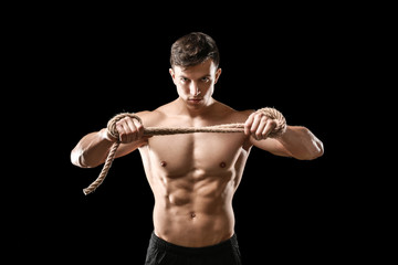 Muscular bodybuilder with rope on dark background