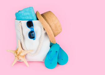 Beach vacation concept with flip-flops and bag on pink background