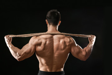 Muscular bodybuilder with rope on dark background, back view