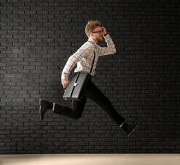 Fototapeta na wymiar Jumping businessman with stylish briefcase on dark brick background