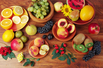 A variety of fruits on the dishes on the table. Grapes, peaches, apples, lemon, orange, pomegranate, pears, plums.