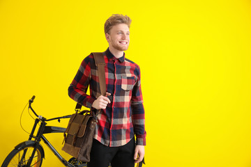 Handsome man with stylish briefcase and bicycle on color background
