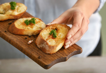 Woman holding board with tasty garlic bread, closeup