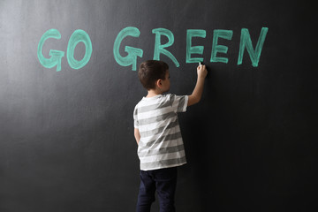 Little boy writing text GO GREEN on dark wall