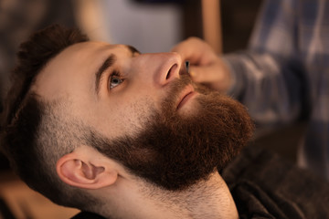 Fototapeta na wymiar Professional hairdresser shaving client in barbershop