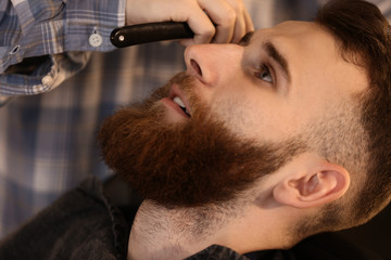 Professional hairdresser shaving client in barbershop