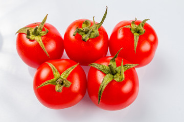 Five delicious ripe tomatoes with green tails in the same plane on a white background