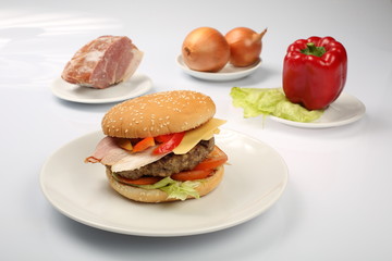 cheeseburger with bacon and beef patty on a plate with vegetables, bell pepper, tomatoes, onions, cucumber, parsley and salad on a white background