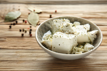 Bowl with tasty feta cheese in olive oil on wooden table