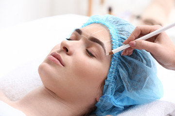 Fototapeta na wymiar Young woman undergoing eyebrow correction procedure in beauty salon