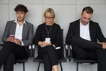 People sitting waiting for a job interview and using social media application on mobile phone. Human resources recruitment concept