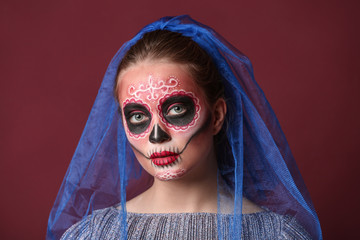 Young woman with painted skull on her face for Mexico's Day of the Dead against color background