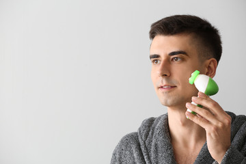 Man with facial massage tool on light background