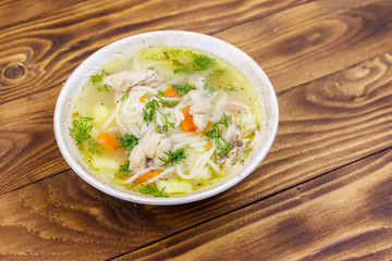 Chicken soup with noodles and vegetables on wooden table