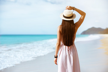 Fototapeta na wymiar Slim lady in dress and hat walks at sea beach