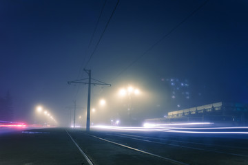 Fototapeta na wymiar road with poles with high-voltage wires and tram tracks or tram rails , evening fog on the streets, poles with high-voltage wires, cityscape with freeze light or light painting