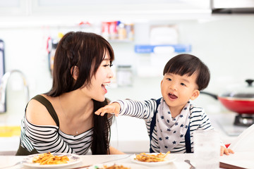 Mother and son in the kitchen, eating noodles together
