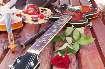 Electric guitar, pipes, maracas and a red rose on a wooden table