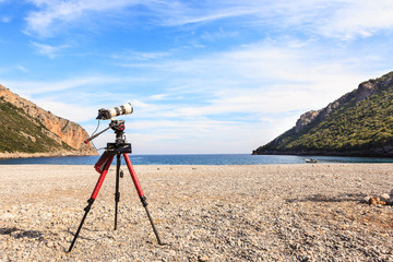 Camera with lens on tripod, greek beach