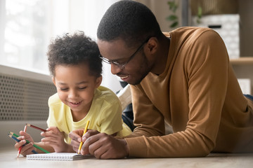 African dad and little toddler son draw with colored pencils