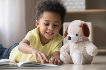 Happy african little boy playing alone reading book to toy