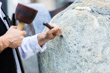 Sculptor with mallet and cutter working on erratic block - obrazy, fototapety, plakaty