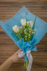 Hand holding a bouquet of white tulips on wooden background