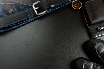 Men's accessories (notebook, pen, phone, shoes, wrist watches, wallet, purse, belt, jeans, pants, shoes) on a black board.