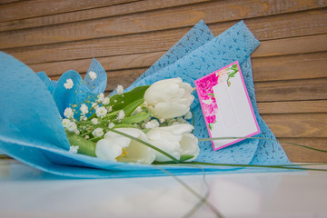 Bouquet of three beautiful white tulips with mockup note on wooden background