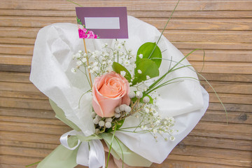 Beautiful bouquet with one rose and a note mockup on wooden background