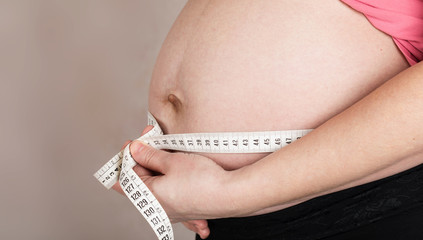 Young pregnant woman measures her belly with  measurement band.