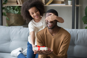 African kid daughter closing eyes congratulating dad giving gift box 