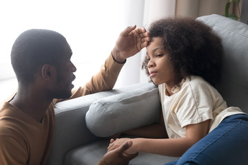 Caring african father touching forehead of ill kid daughter