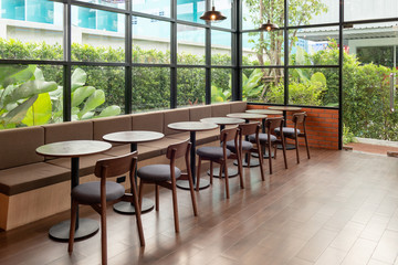 Rows of wooden table and chair inside of glass room with garden